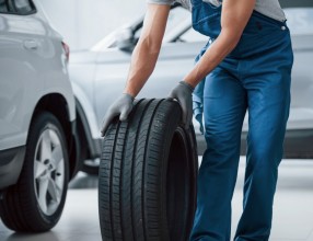 On my way. Mechanic holding a tire at the repair garage. Replacement of winter and summer tires