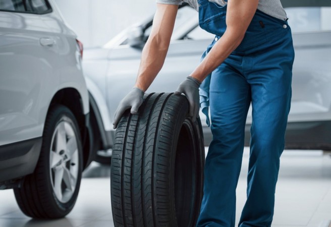 On my way. Mechanic holding a tire at the repair garage. Replacement of winter and summer tires
