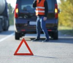 Red warning triangle on asphalt road. Tow truck worker near broken down car