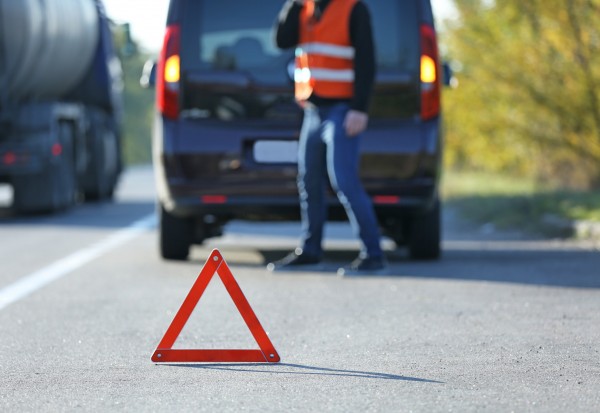 Red warning triangle on asphalt road. Tow truck worker near broken down car
