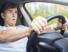 Handsome frightened fearful guy, driver, young scared man shocked about to have traffic accident, driving car on road holding steering wheel of automobile. Unfastened by a seat belt. Traffic violation