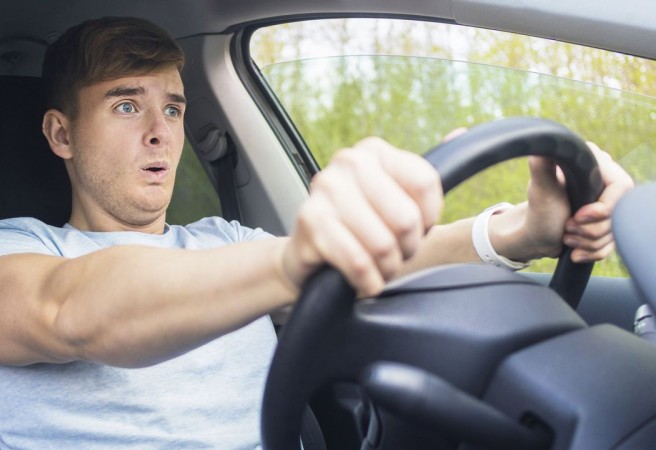 Handsome frightened fearful guy, driver, young scared man shocked about to have traffic accident, driving car on road holding steering wheel of automobile. Unfastened by a seat belt. Traffic violation