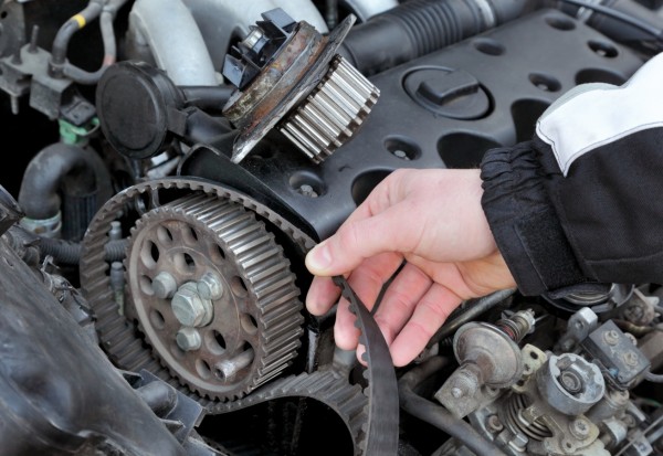 Car mechanic replacing timing belt at camshaft of modern engine