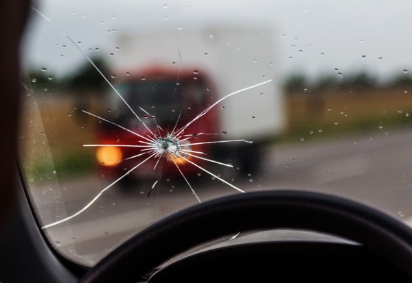 Broken windshield of a car. A web of radial splits, cracks on the triplex windshield. Broken car windshield, damaged glass with traces of oncoming stone on road or from bullet trace in car glass